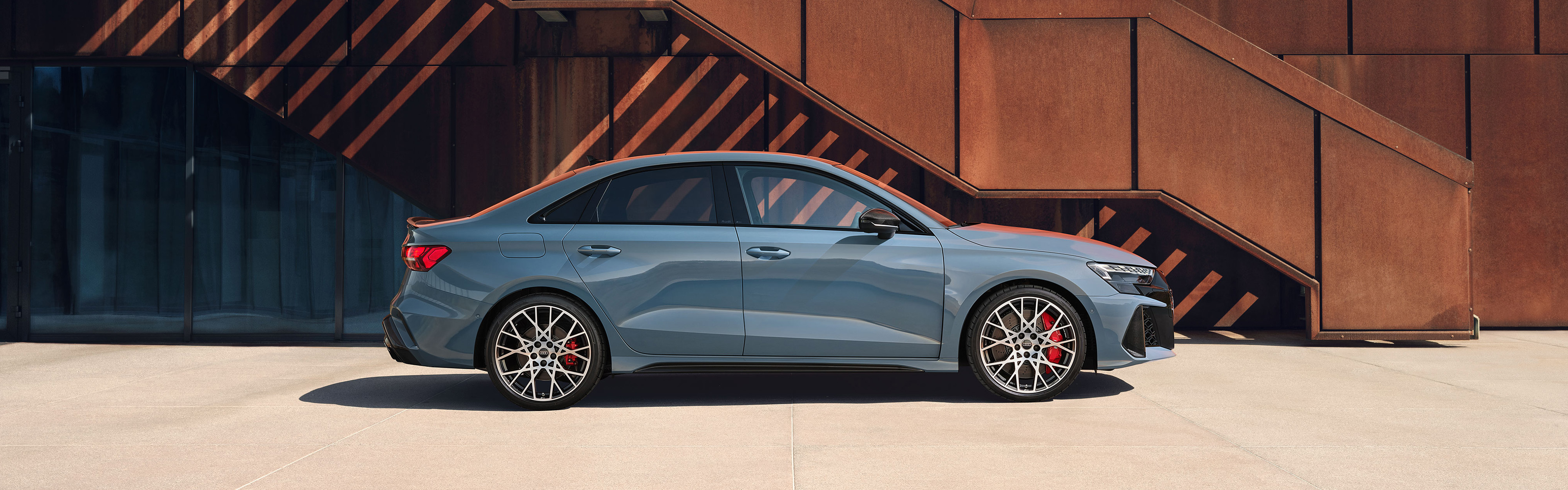 Die grauer Audi RS 3 Limousine in der Seitenansicht vor einer Stahlkulisse