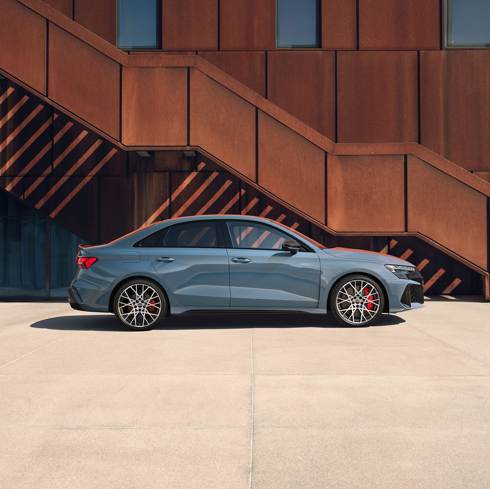 Die grauer Audi RS 3 Limousine in der Seitenansicht vor einer Stahlkulisse