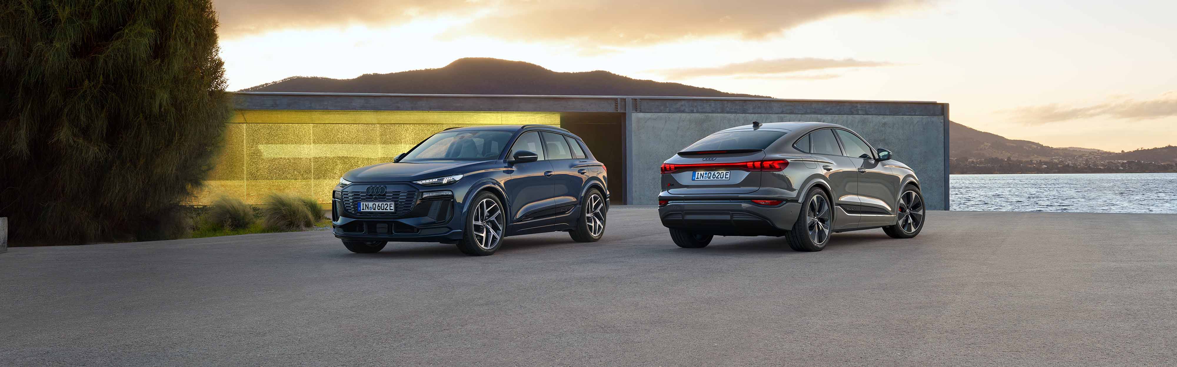 Zwei Audi Q6 Sportback e-tron seitliche Heckansicht und seitliche Frontansicht, vor einem futuristischen Geb&auml;ude am Meer
