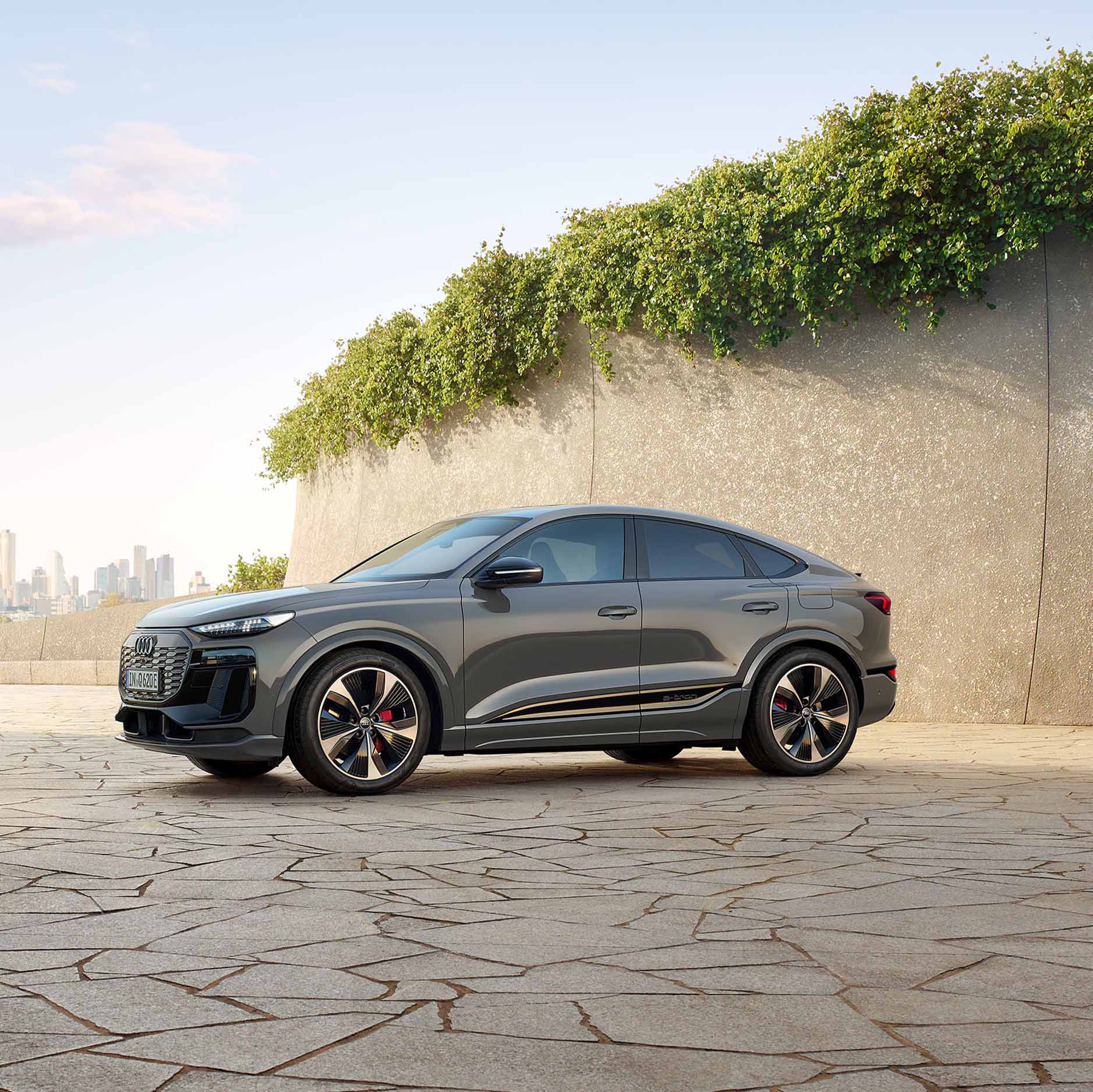 Der neue Audi Q6 Sportback e-tron in der Seitenansicht zwischen zwei Steinigen Bergen. Im Hintergrund eine Stadt