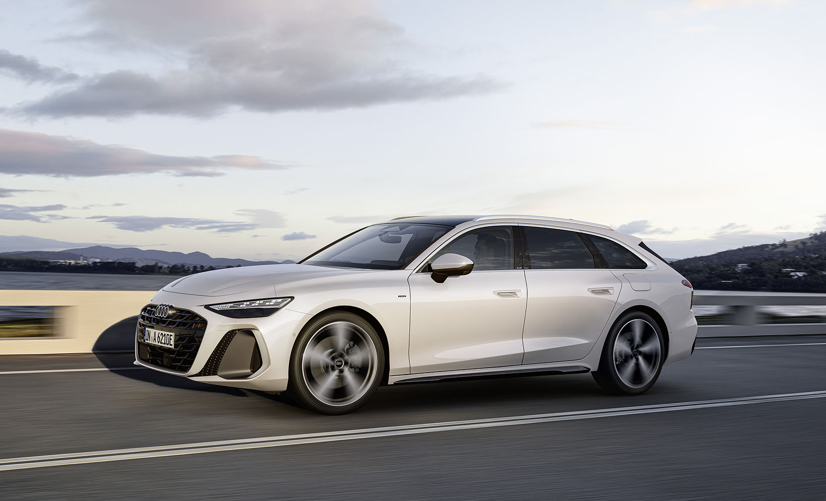 Ein wei&szlig;er Audi A6 Avant e-hybrid in der Dreiviertelansicht von vorn, fahrend an einer Hangstra&szlig;e
