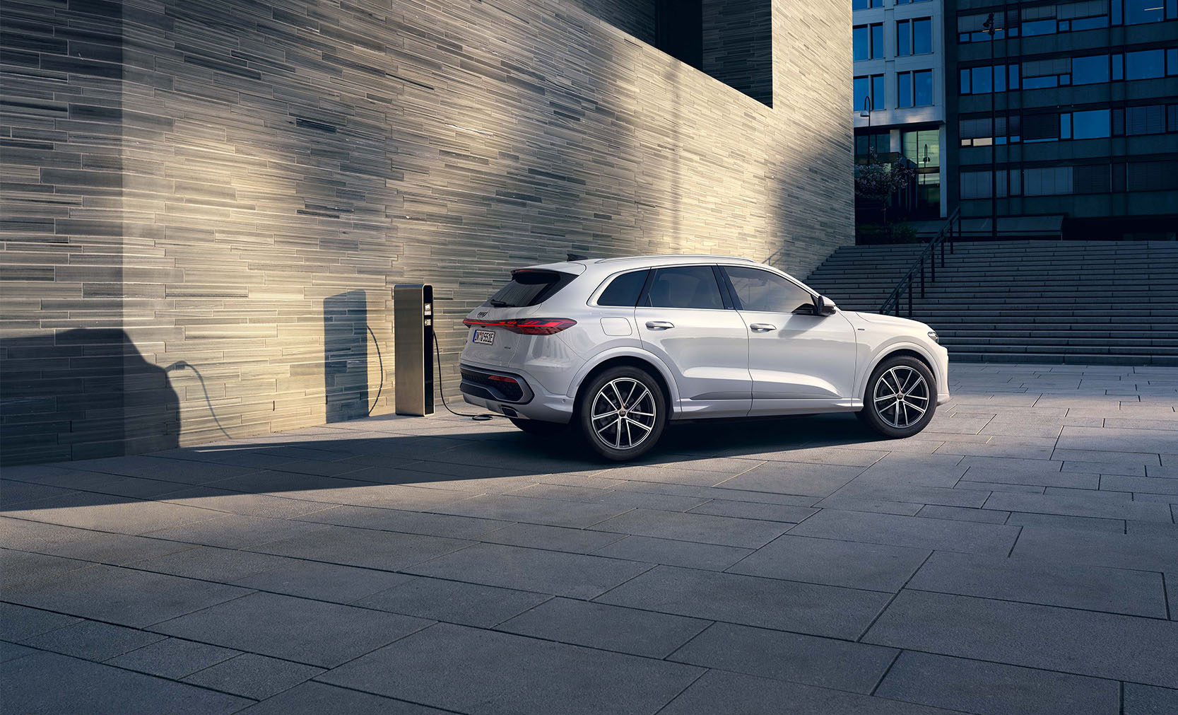Ein wei&szlig;er Audi Q5 SUV e-hybrid seitlich vor einer Betonwand