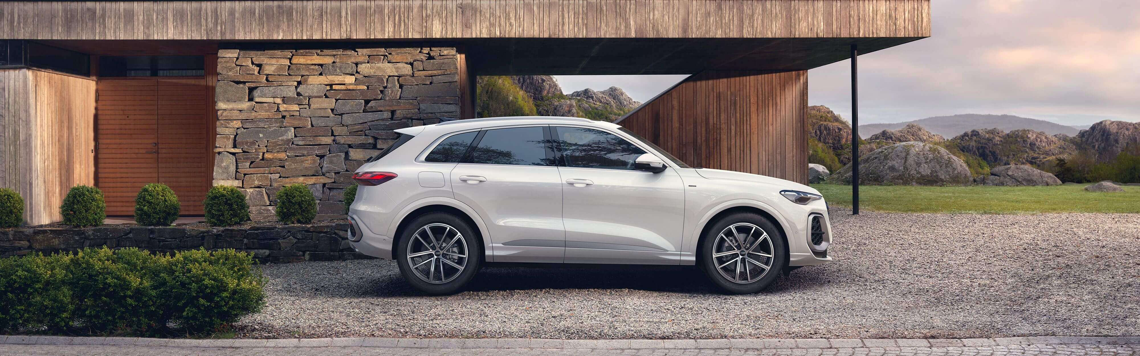 Der wei&szlig;er Audi Q5 SUV e-hybrid in der Seitenansichtnsicht vor einem futuristischen Haus