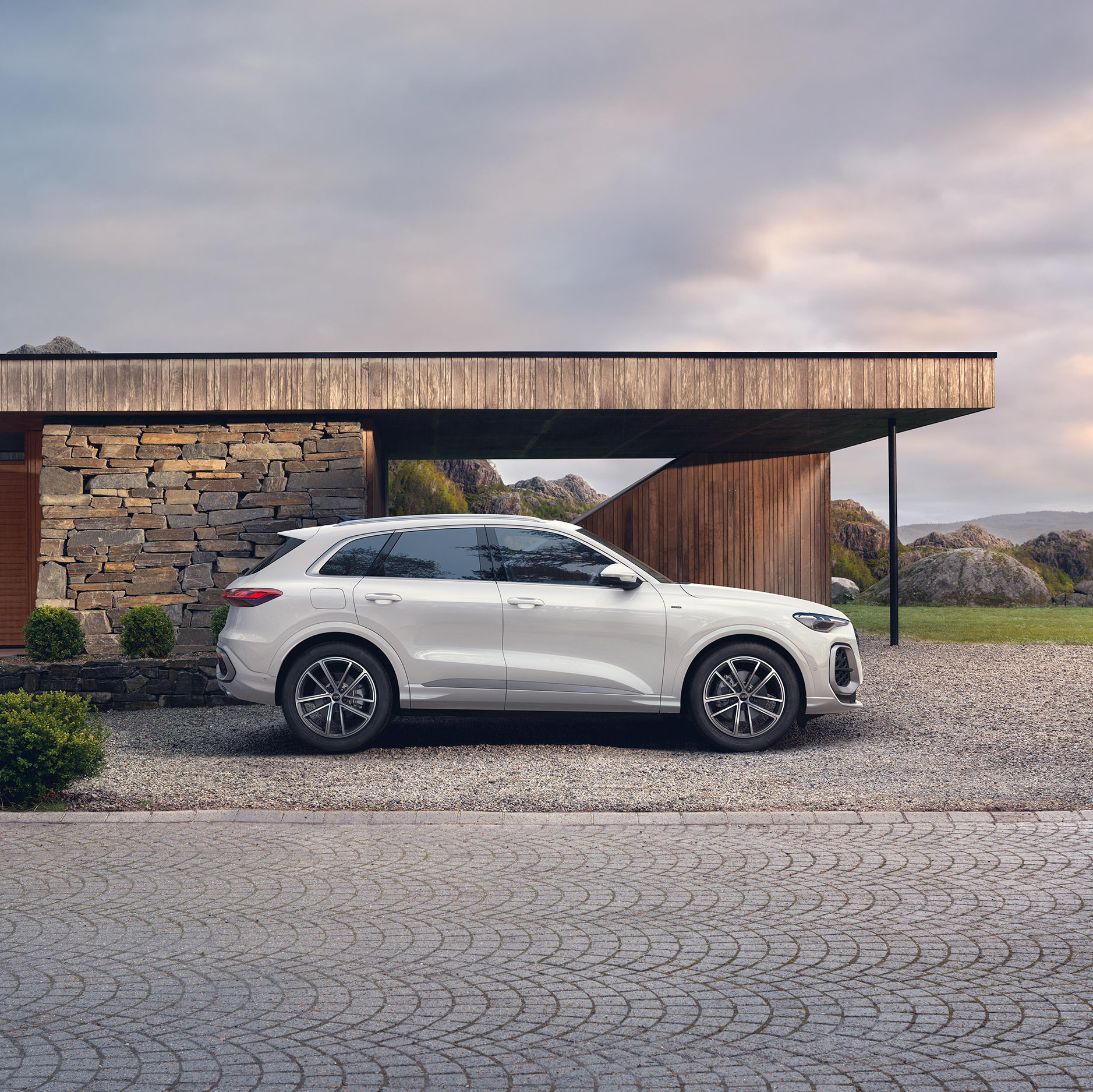 Der wei&szlig;er Audi Q5 SUV e-hybrid in der Seitenansichtnsicht vor einem futuristischen Haus