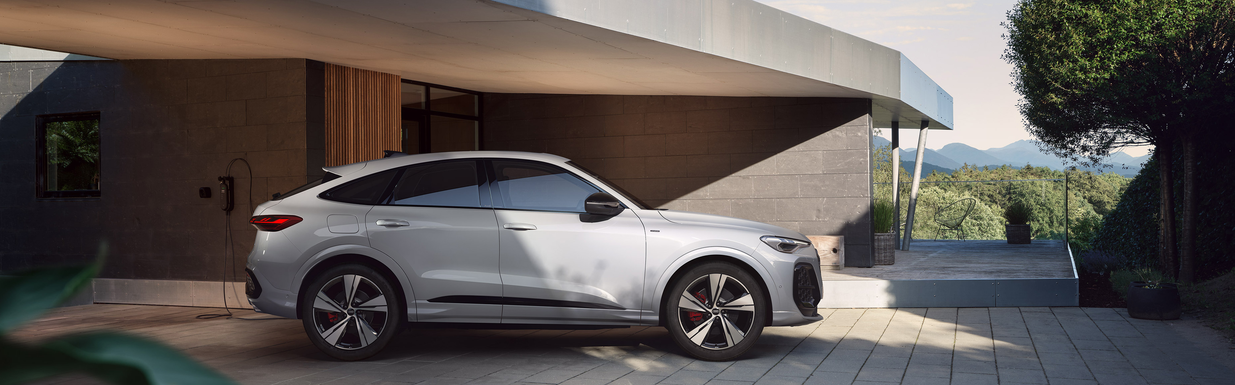 Der wei&szlig;er Audi Q5 SUV e-hybrid in der Dreiviertelansicht vor einem futuristischen Haus