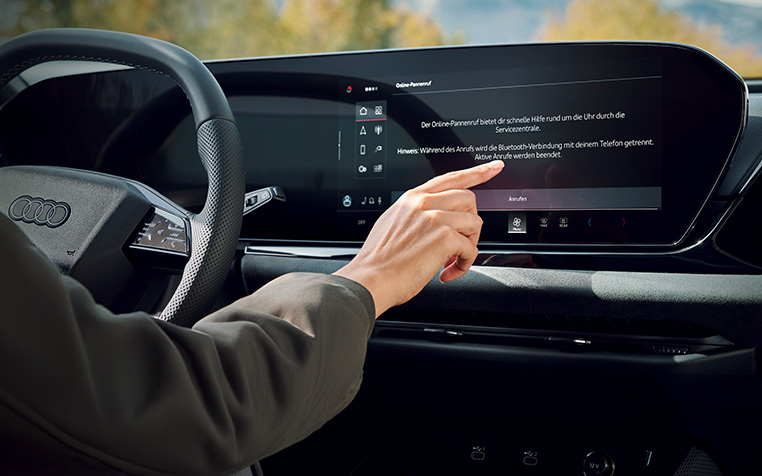 Eine Frau sitzt in einem Audi und dr&uuml;ckt auf dem MMI die Schadenmeldung. 
