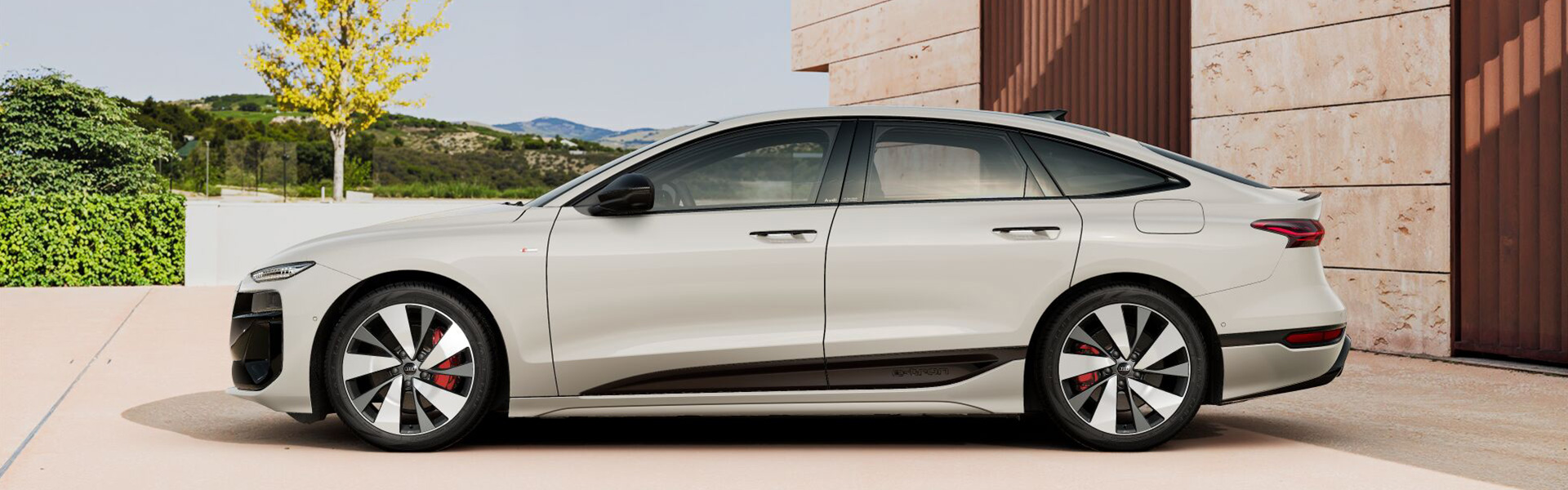 Ein Audi A6 Sportback e-tron in Siambeige Metallic in Hauseinfahrt vor Garten
