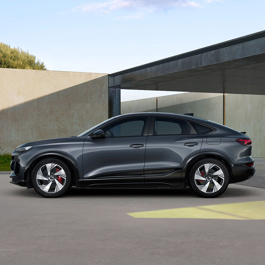 Der Audi SQ6 Sportback e-tron in Daytonagrau Perleffekt seitlich vor Geb&auml;ude mit Carport